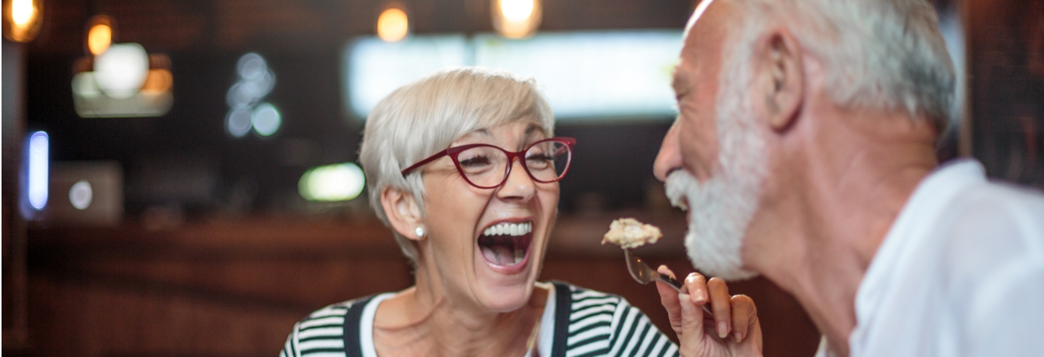 senior-woman-laughing-while-feeding-her-male-partner-in-the-picture-2048x700jpg.jpg
