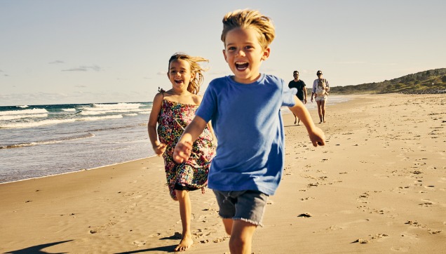 Two kids running on the beach and smiling