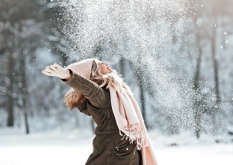 A woman smiling and throwing snow in the air