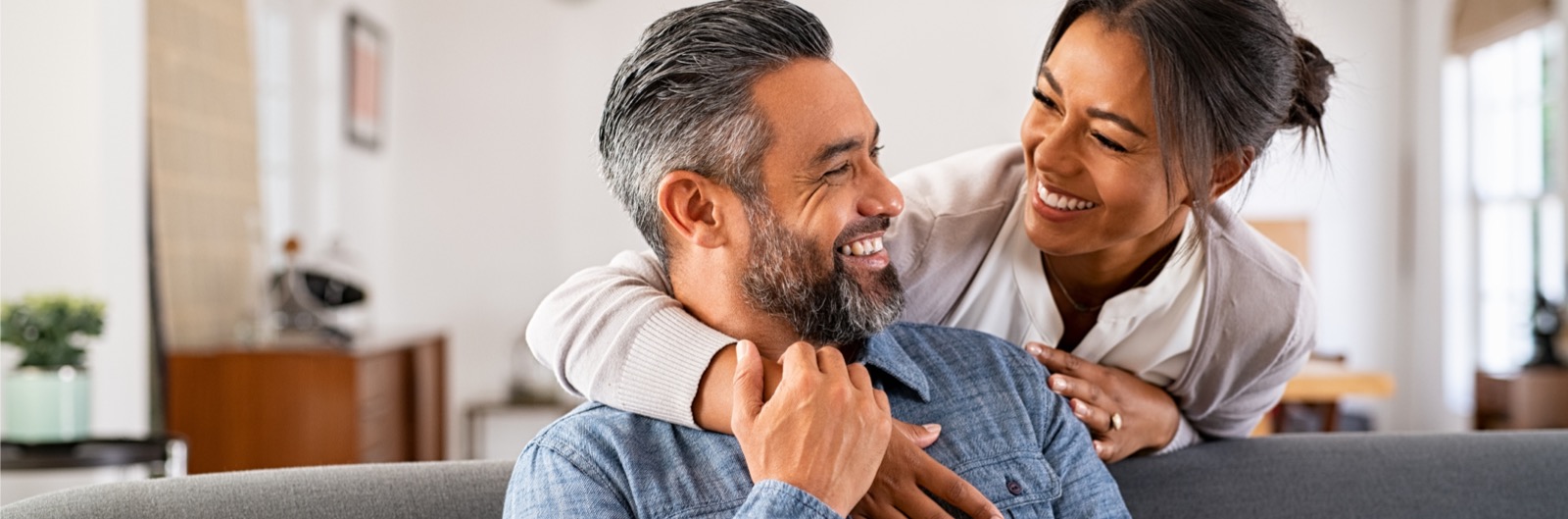 mature-multiethnic-couple-laughing-and-embracing-at-home-picture-1600x529.jpg