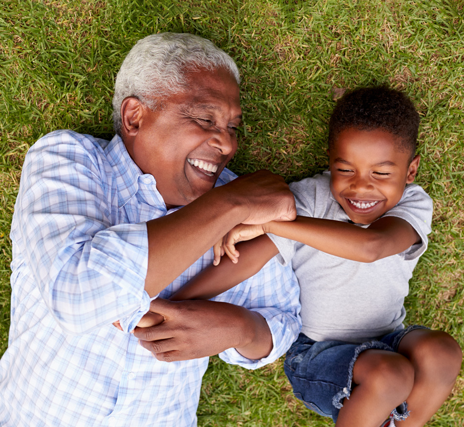 An older man and young boy laying on the grass smiling