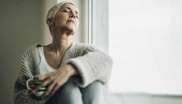A women sitting next next to a window with her eyes closed