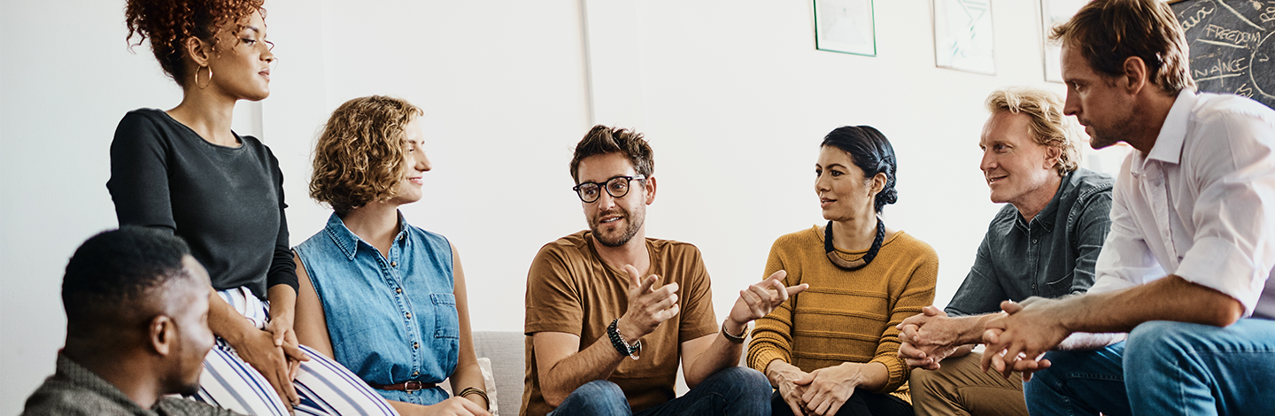 A group of employees sitting around a couch listening to one person talk