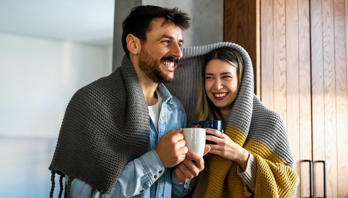A couple sharing a blanket and drinking from mugs