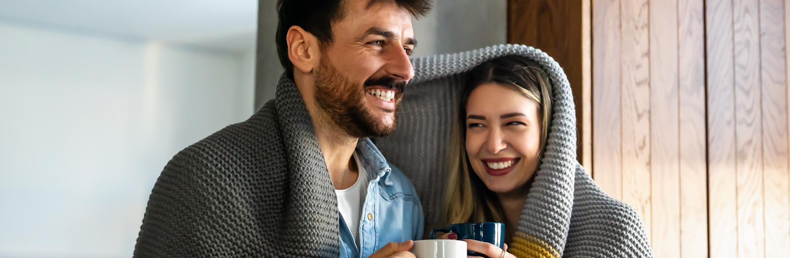 A couple sharing a blanket and drinking from mugs