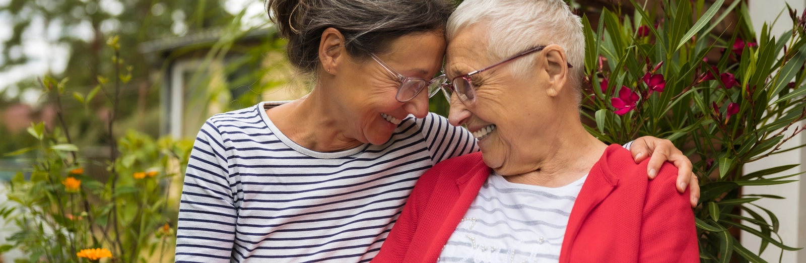 A daughter and older mother sitting in a garden and laughing