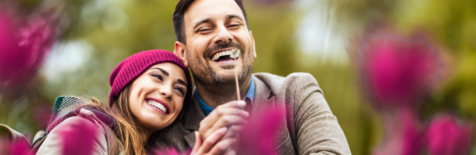 A happy couple sitting outdoors surrounded by blurred pink flowers