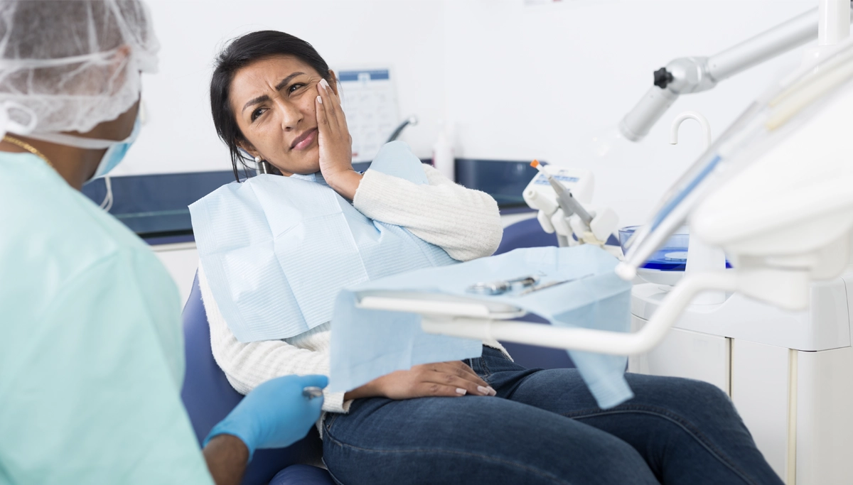A woman with a cavity sitting in a dental chair, holding her jaw with a pained expression