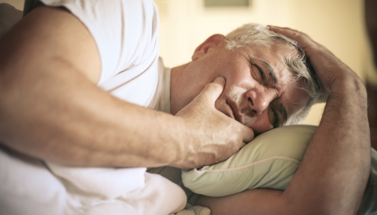 A man laying in bed and holding his jaw in pain