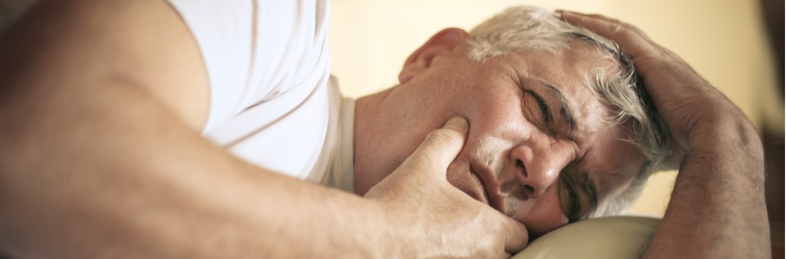 A man laying in bed and holding his jaw in pain