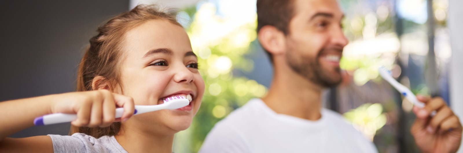 A dad and daughter brushing their teeth