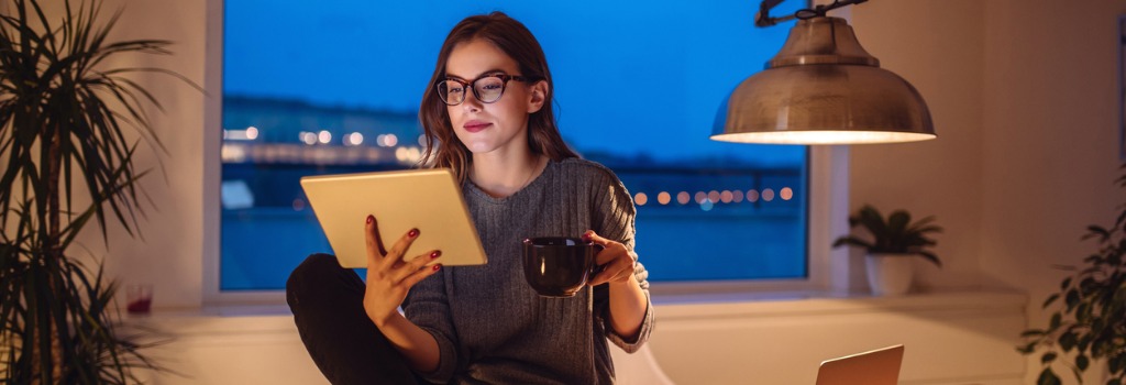 A person drinking coffee and looking at a tablet