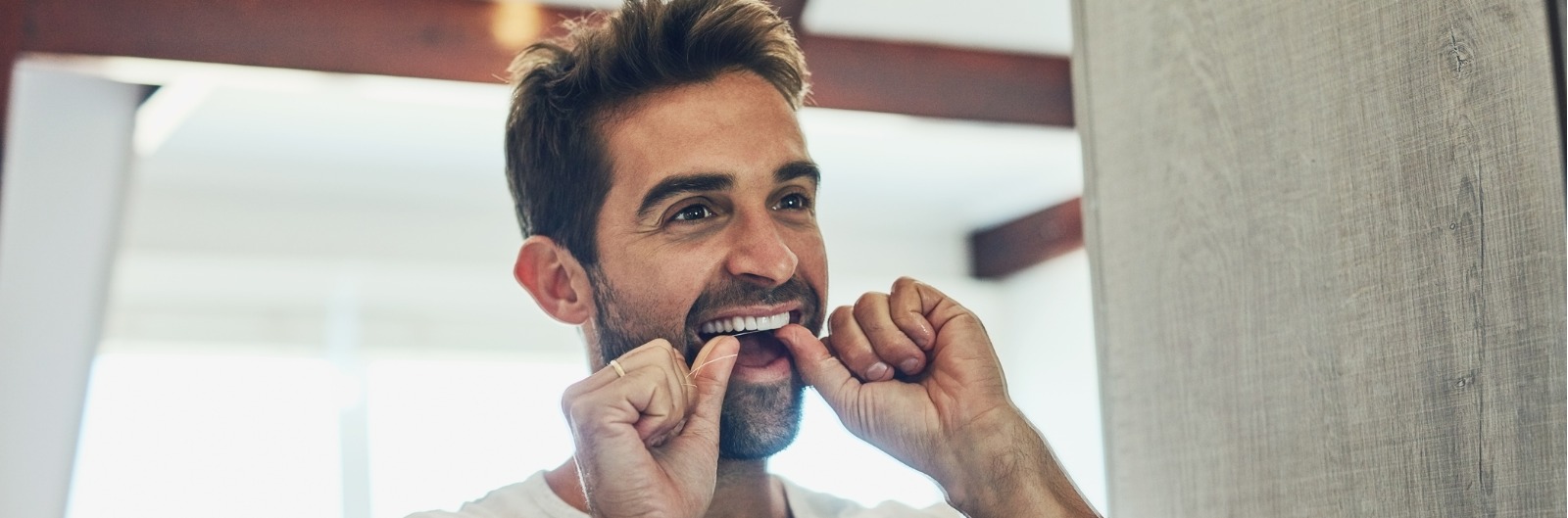 A man flossing his teeth in a mirror