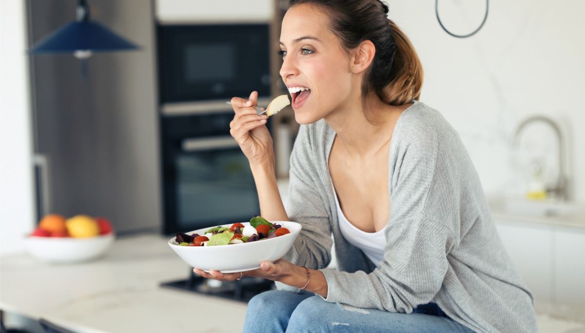 A woman eating a salad in her kitchen
