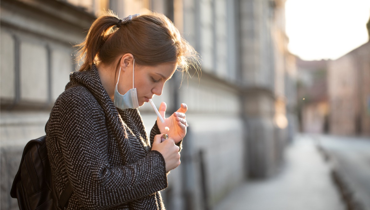 A woman lighting a cigarette outside on the street