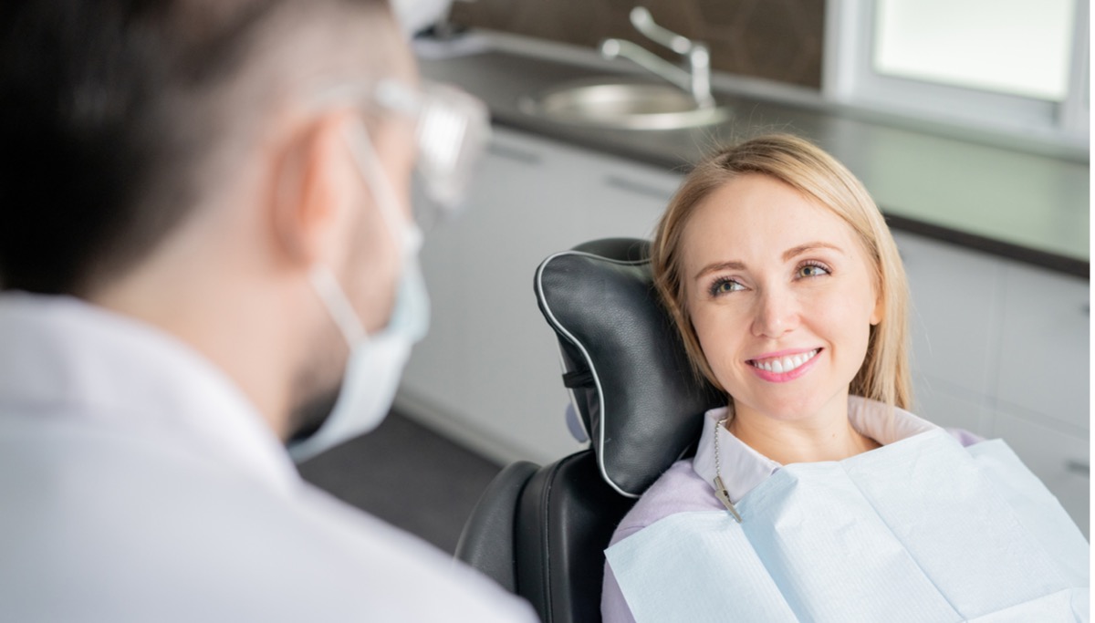 happy-young-blonde-female-patient-looking-at-her-dentist-with-healthy-picture-1200x683.jpg