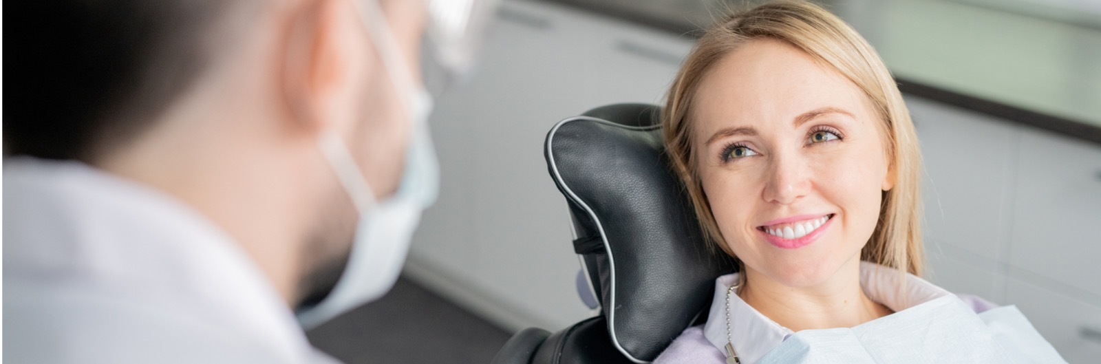 happy-young-blonde-female-patient-looking-at-her-dentist-with-healthy-picture-1600x529.jpg