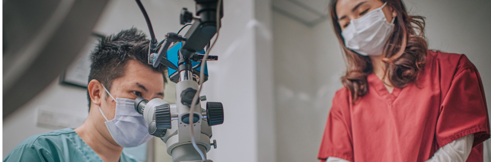 asian-chinese-male-dentist-looking-through-microscope-on-patients-in-picture-1600x529.jpg