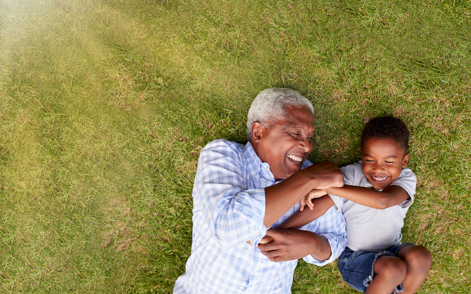 An older man and young boy laying on the grass smiling