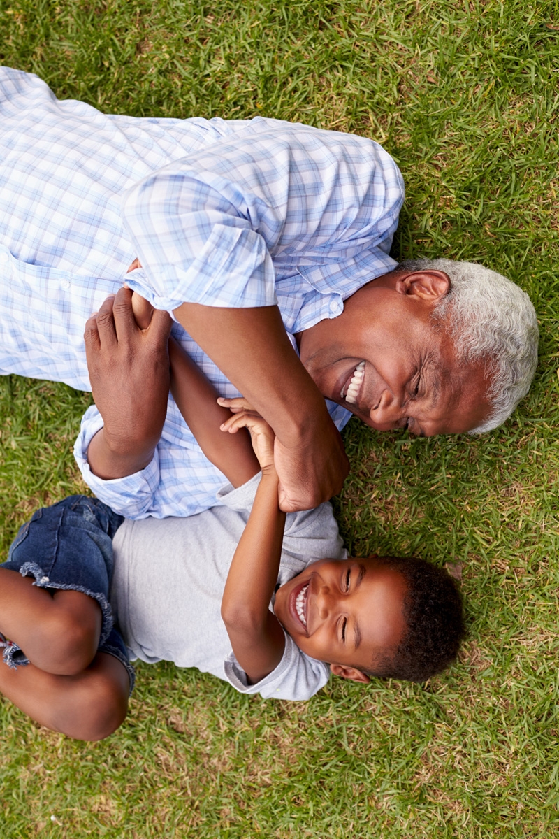 An older man and young boy laying on the grass smiling