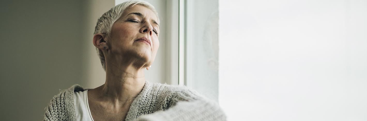A woman sitting next to a window with her eyes closed