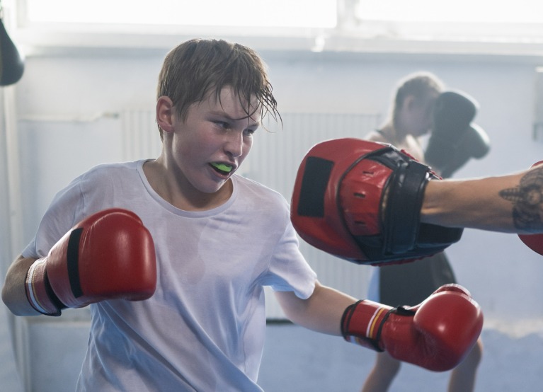 Young male boxer with a mouth guard sparing with his adult coach
