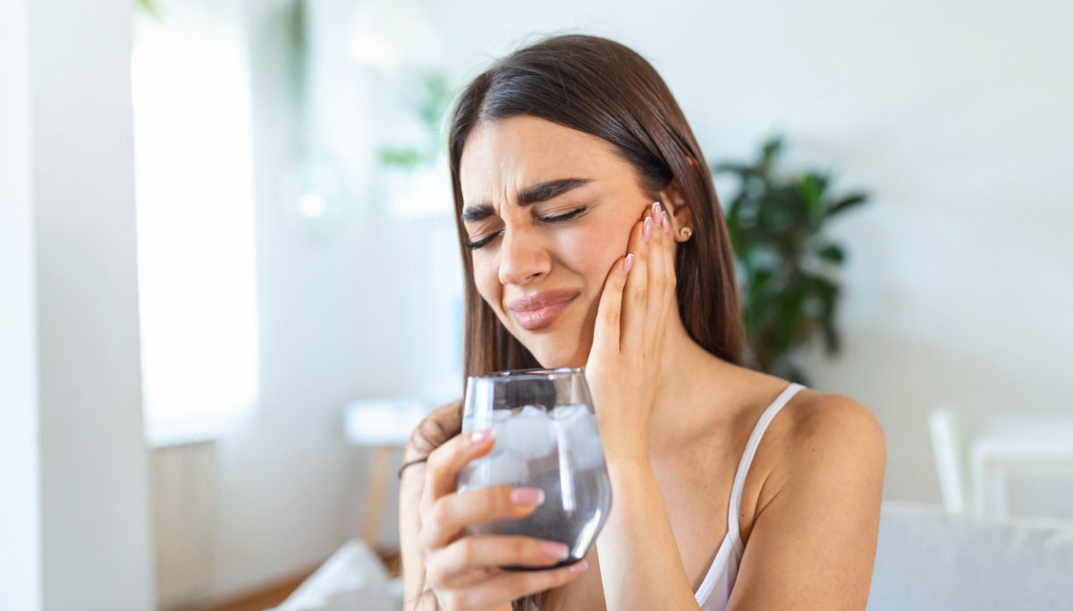A woman holding a glass of water and grimacing in pain