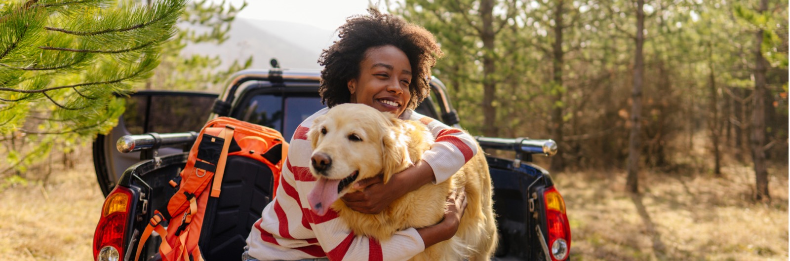 A woman sitting in the back of a pickup truck and holding a dog