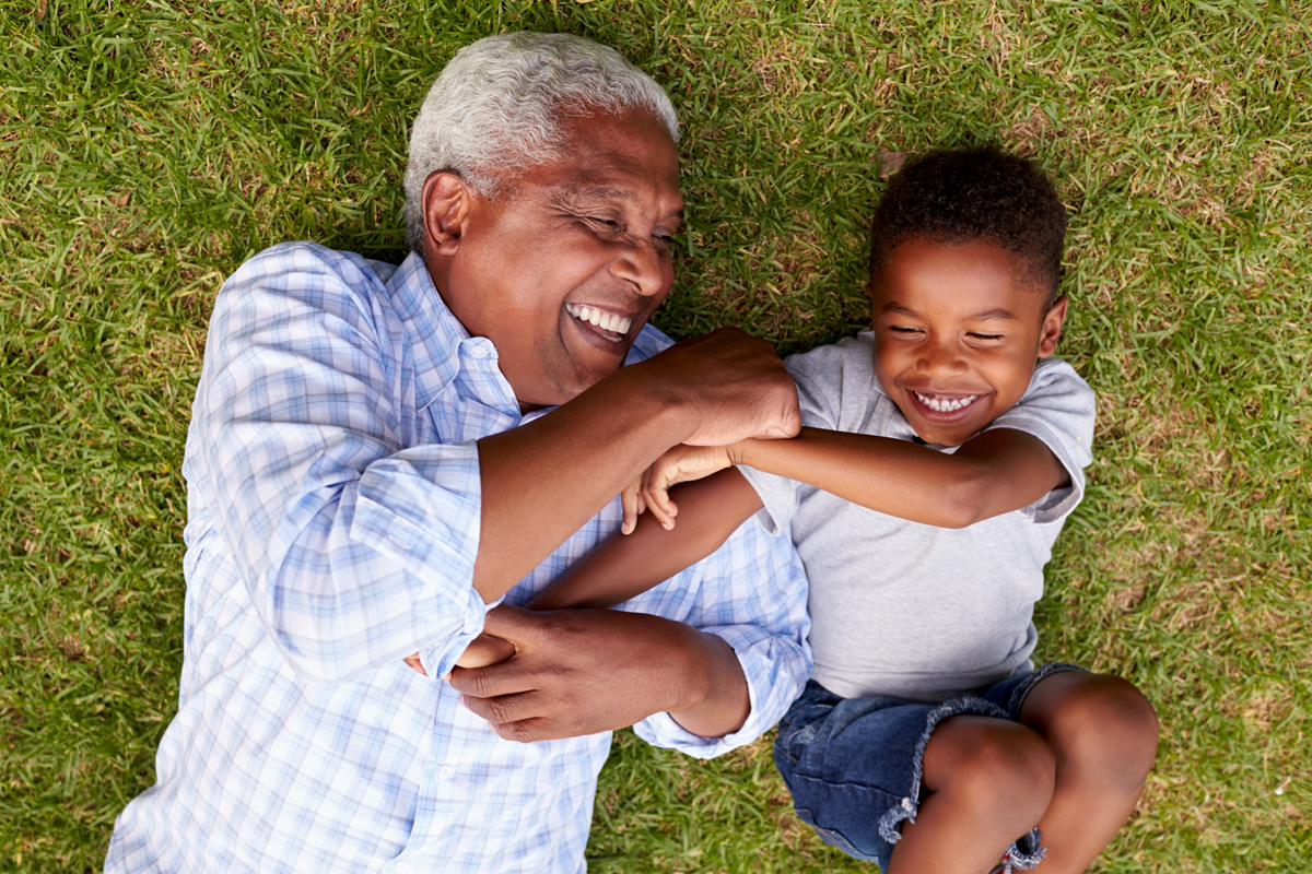 An older man and young boy laying on the grass smiling