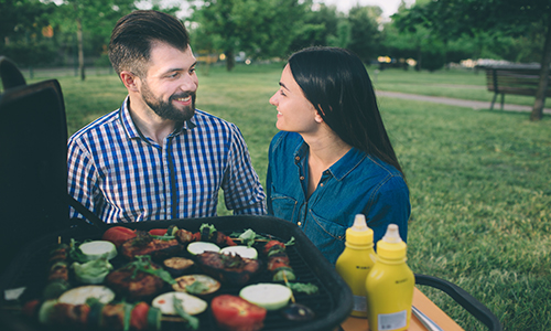 Friends making barbecue and having lunch in the nature. Couple having fun while eating and drinking at a pic-nic - Happy people at bbq party