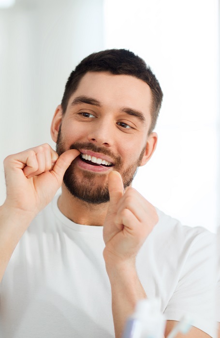 man with dental floss cleaning teeth at bathroom