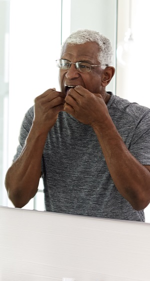 Senior Man Flossing Teeth Looking At Reflection In Bathroom Mirror Wearing Pajamas