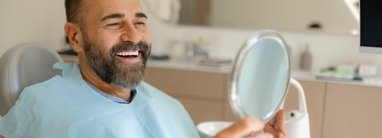 man-smiling-in-mirror-at-dentist-1600x578.png